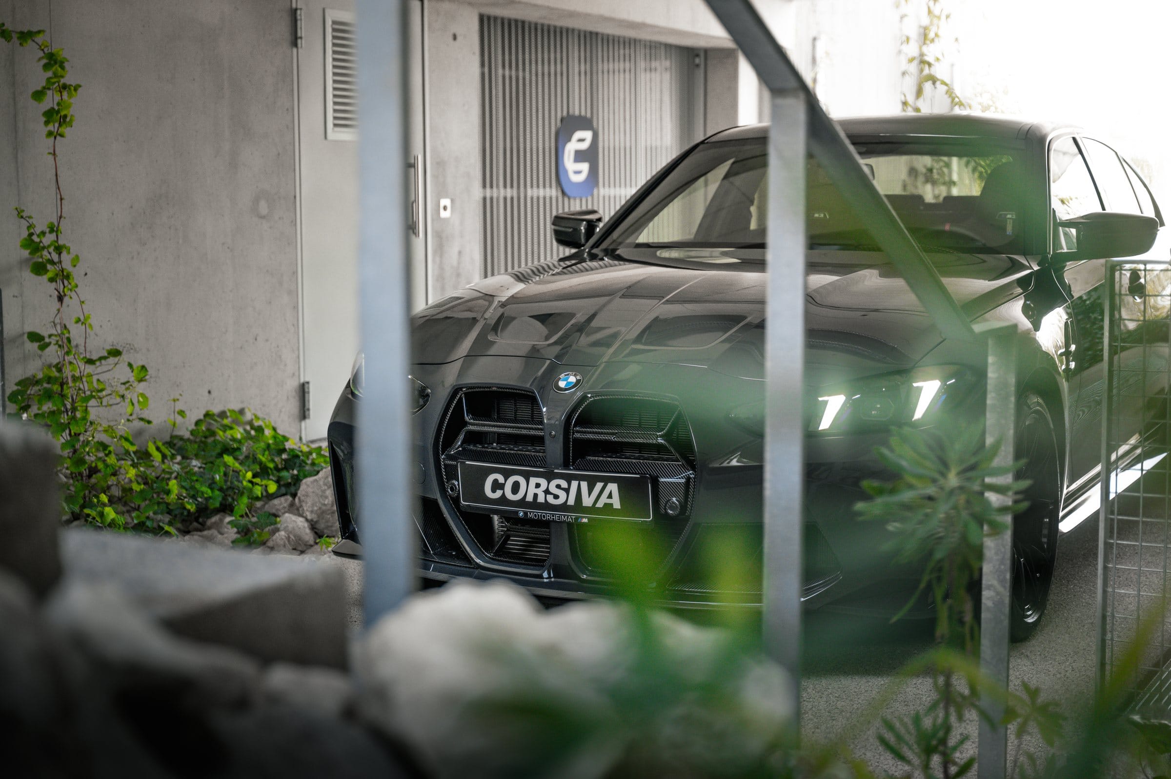 Calandre de la BMW M3 Competition du groupe Corsiva, derrière la végétation du garage