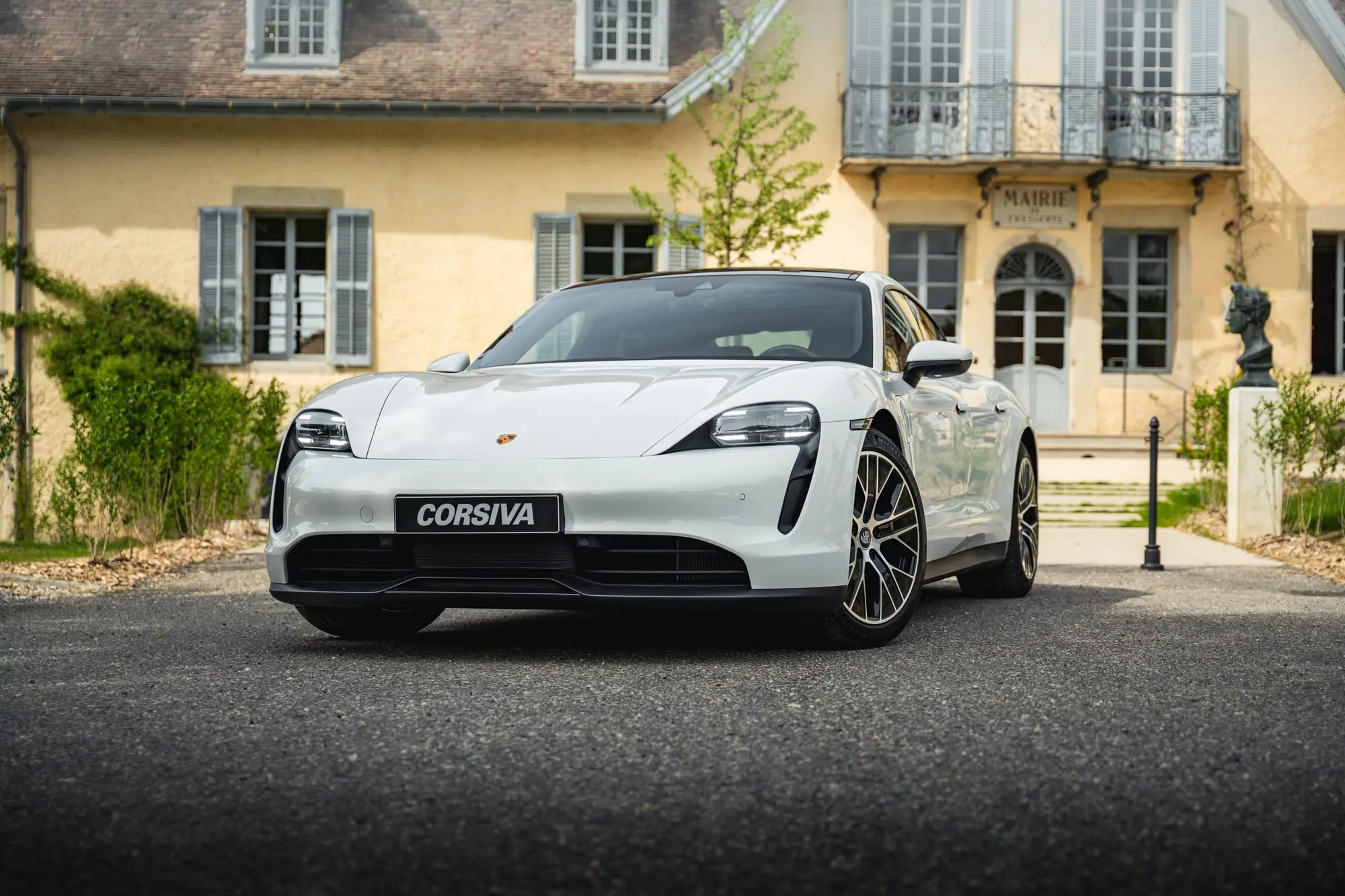 Porsche Taycan blanche du groupe Corsiva devant une maison de maître