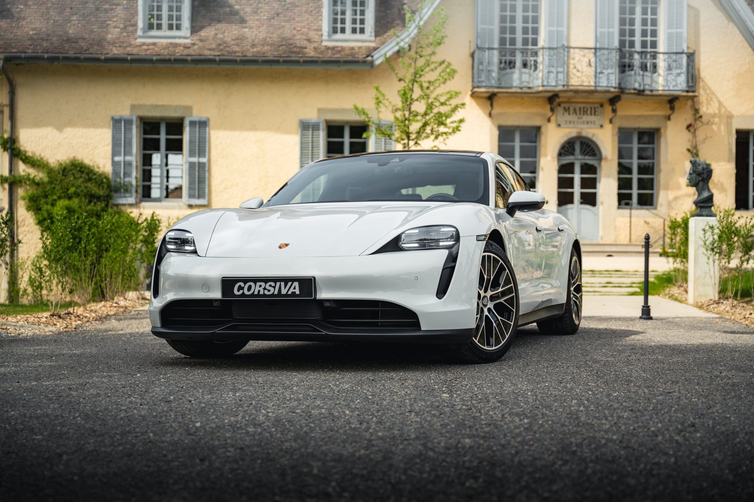Porsche Taycan blanche du groupe Corsiva devant une maison de maître